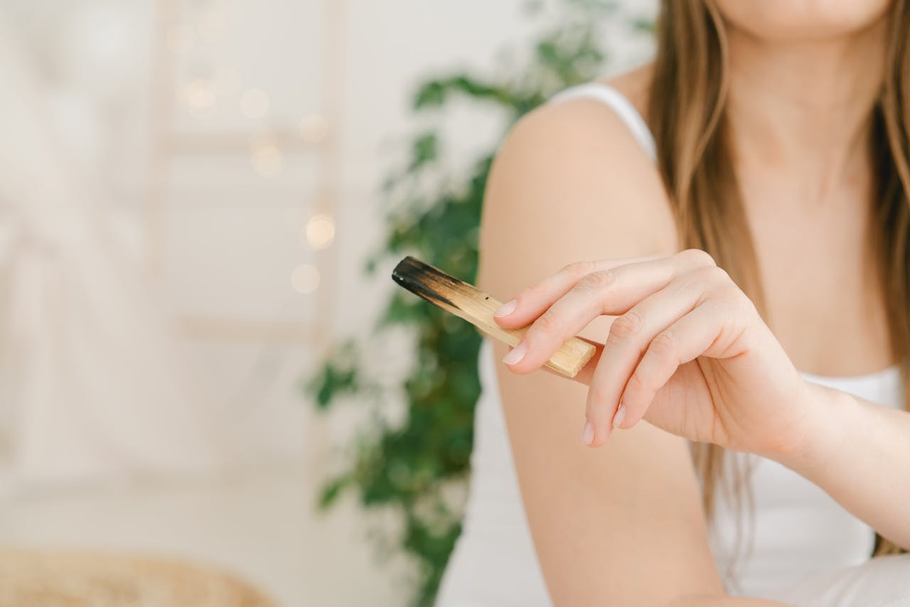 A woman in a calm setting holding a Palo Santo stick, embodying relaxation and mindfulness.